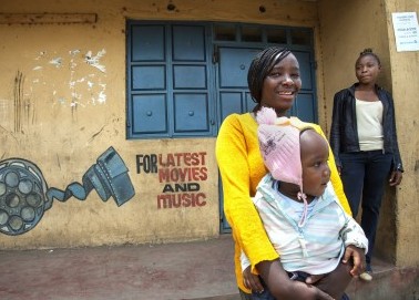 Halima, a young mother and business woman, holding her son outside her movie and DVD shop