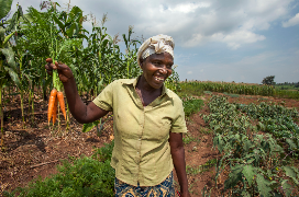 Gloria, a farmer, standing in front of her crops holding a bunch of carrots. 