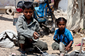 Two indian children sitting in the street playing with bicycle parts. 