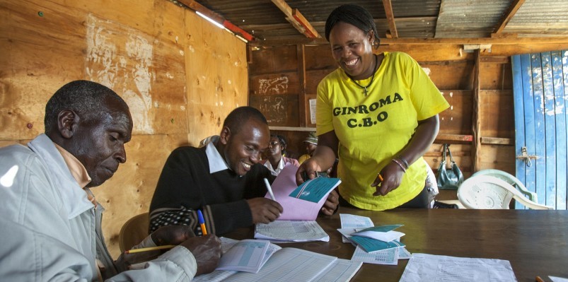 Beatrice Wanjiku shows her savings book to her Self-Help Group treasurer (far left) | Yogurt Maker | Nairobi outskirts