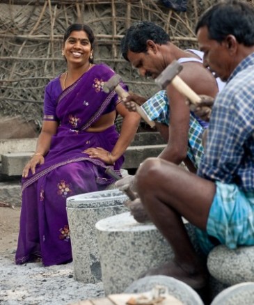 Padmavathi, a sculptor from Kanchipuram, India, sitting on a rock sculpture whilst two other men are working. 