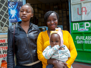 Irene, Halima and Helima's child standing in front of their music and movie shop.